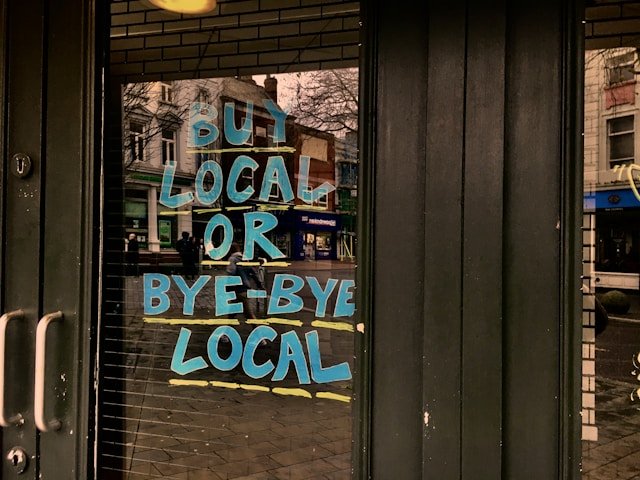 Door to a store front that has marker written on the door writting out "shop local or bye bye local"